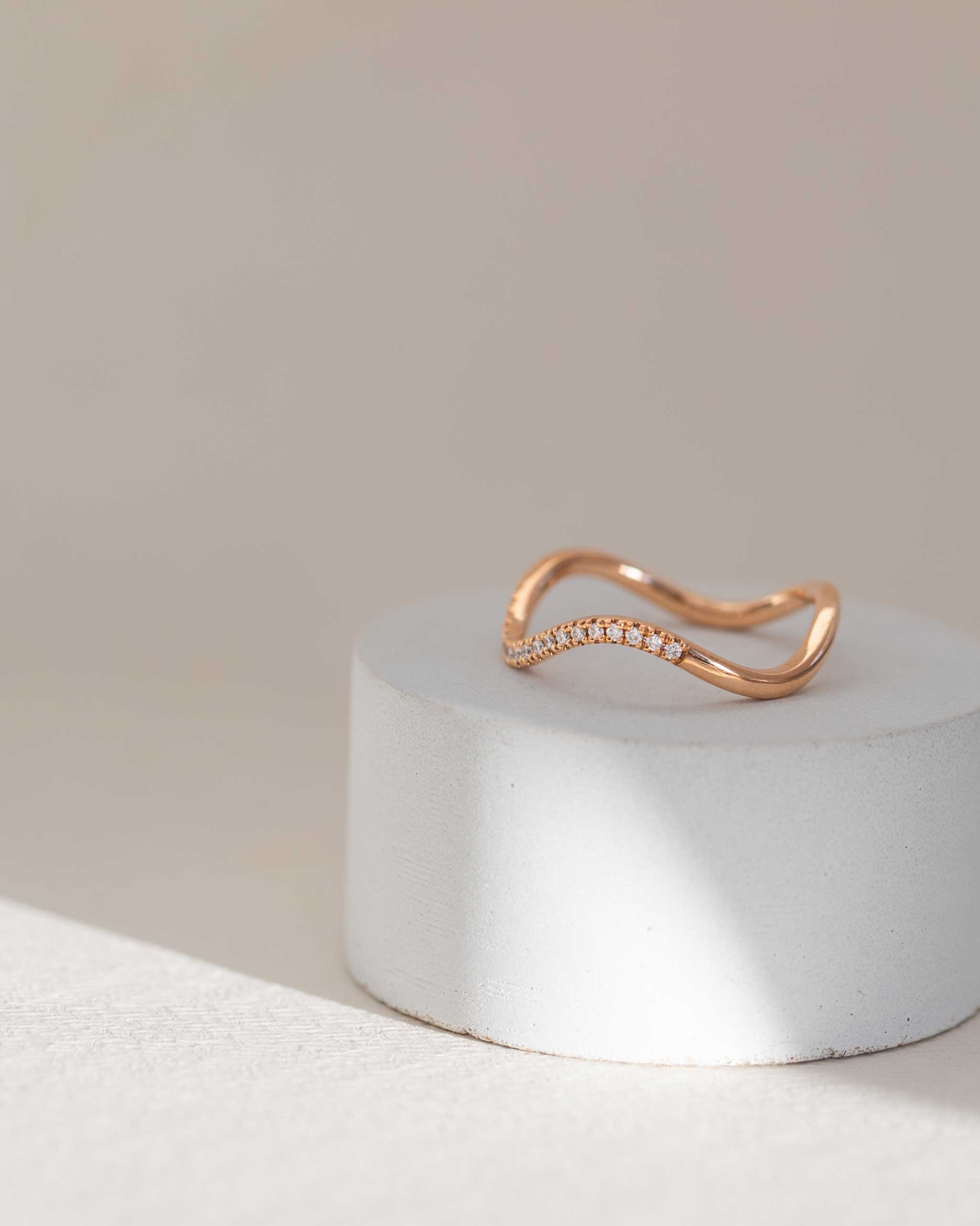 Yellow gold wave ring on a white stone surface with a light gray background